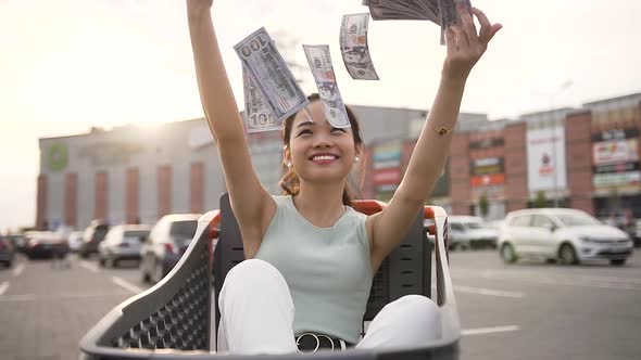 Funny Young Pretty Vietnamese Girl Sitting in the Market Trolley and Scattering Cash