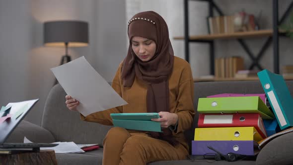 Focused Serious Woman in Hijab Using Tablet and Graph Analyzing Company Strategy Sitting in Home