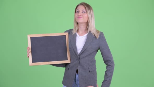 Happy Young Blonde Businesswoman Holding Blackboard and Giving Thumbs Up