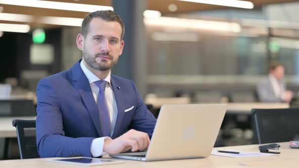 Thumbs Down By Middle Aged Businessman with Laptop at Work