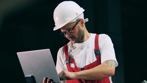 Male Technician in a Hardhat Is Operating a Laptop