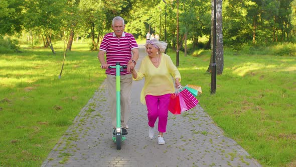 Senior Stylish Couple Grandmother Grandfather After Shopping with Bags Using Scooter for Riding