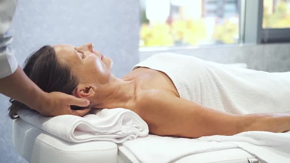 Aging Woman Is Horizontal Lying on the Massage Table and Getting Professional Head Touching