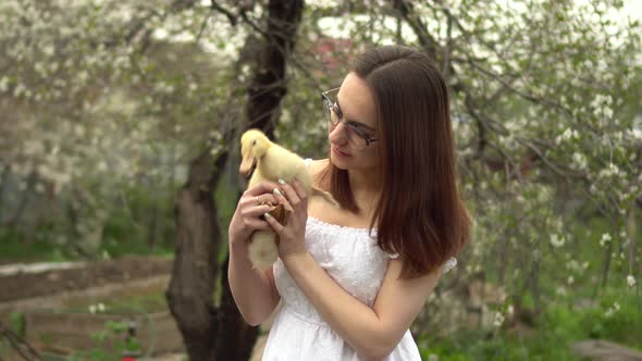 A Young Woman in a White Dress Holds a Real Duckling in Her Arms
