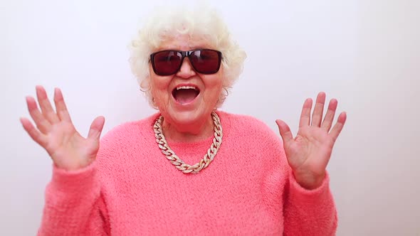 Portrait of Funny Amazed Surprised Senior Blonde Woman in Sun Glasses and Pink Sweater on White