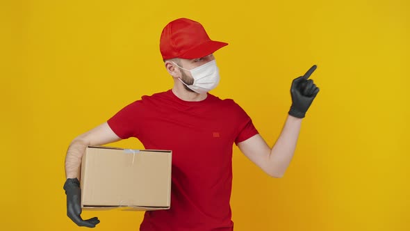 Positive Courier Wearing Protective Mask Holding Cardboard Box and Indicating Aside at Free Space