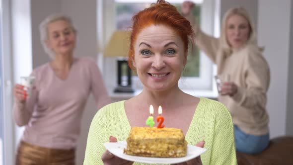 Joyful Redhead Beautiful Woman with Birthday Cake Blowing Out 42 Years Candles Smiling Looking at
