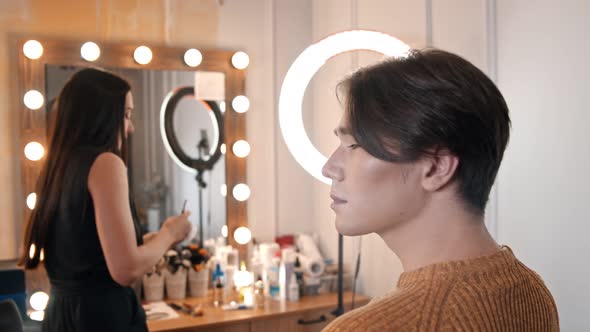 Woman Make Up Artist Applying Highlights on a Face of Male Model Using a Brush