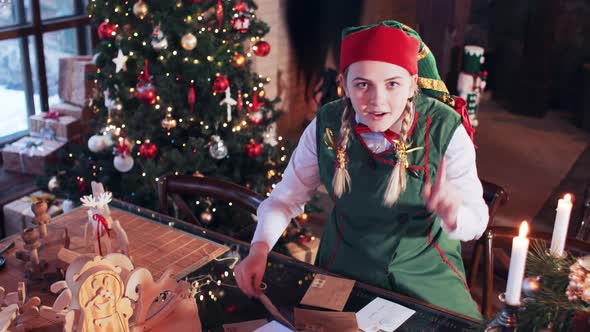 Merry elf girl in a green suit transfers letters on a table