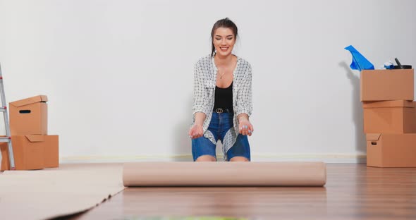 A Young Woman Unfolds a Roll of Construction Cardboard to Protect the Floor From Painting