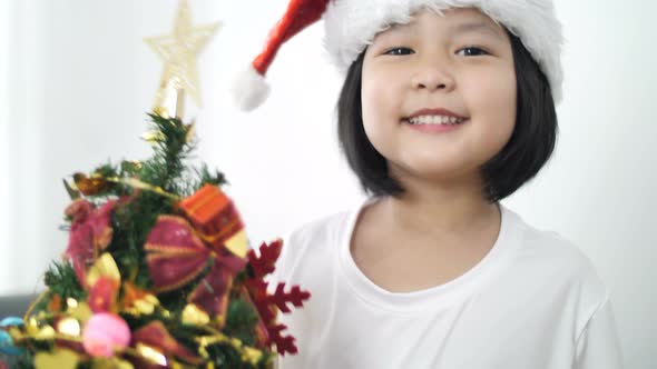 Happy lovely Asian girl putting ornament on Christmas tree and showing all together.