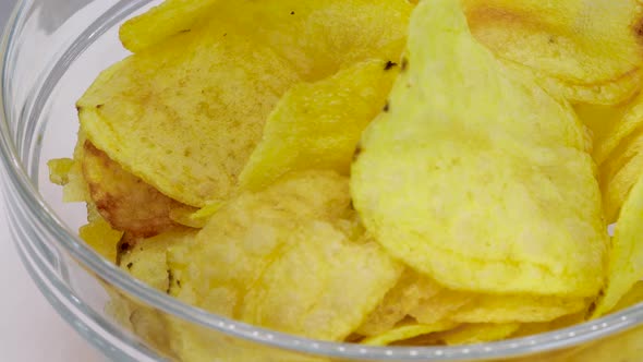 Pile of potato chips into transparent glass bowl, macro shot in 4k. Close up view.