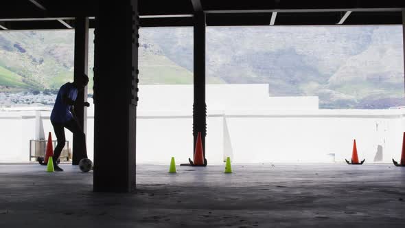 African american man doing slalom with a football in an empty urban building