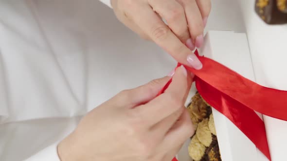 Vertical Shot Closeup Chocolatier Ties Red Bow on Gift Box of Chocolate Handmade Candies