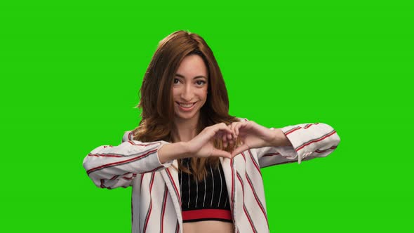 Cute smiling girl pose on green screen showing heart and thumb up gestures