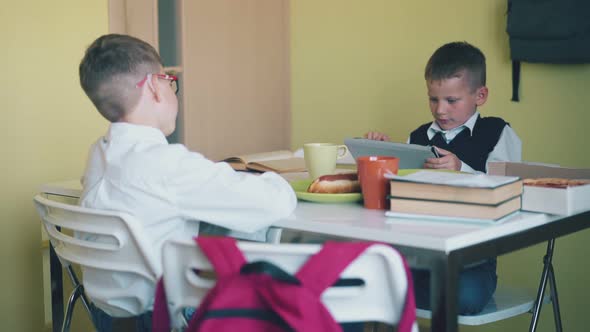 Little Boy Plays on Tablet Schoolmate Sits at White Table