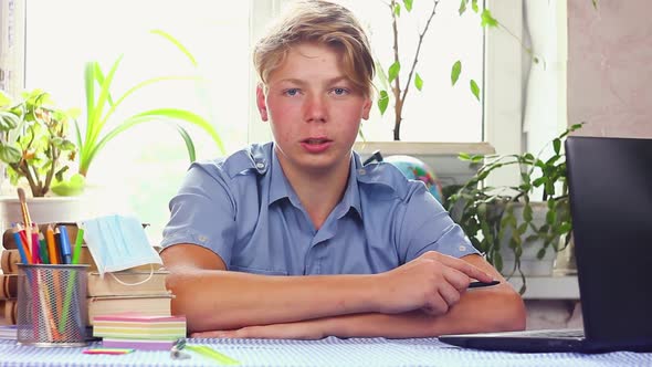 Young Teenager in a Blue Shirt European Appearance Sits at a Work Table 