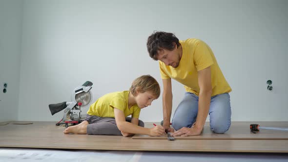 Father and His Little Son Install Laminate on the Floor in Their Apartment