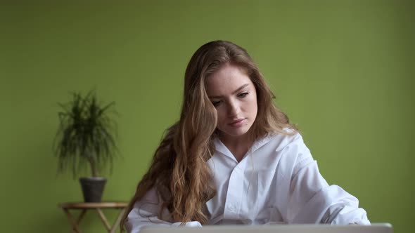 Young Girl Uses Laptop While Sitting On Bed In Apartment.