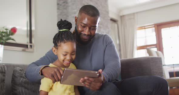 Happy african american daughter and father using tablet on sofa