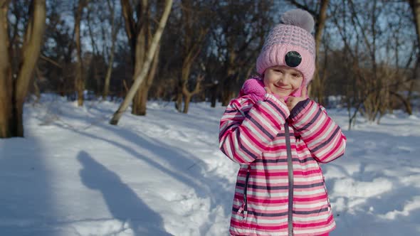 Joyful Little Child Girl Smiling Showing Thumbs Up Gesture on Snowy Road in Winter Park Outdoors