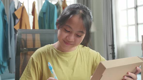 Asian Young Girl Online Seller Look At The Package And Write While Selling Clothes At Home