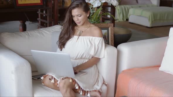 Pretty Woman with Laptop Sitting in Chair in Resort Lounge