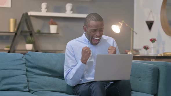 African Man with Laptop Celebrating Success on Sofa