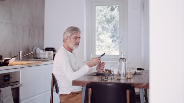 Mature man using smartphone at breakfast table