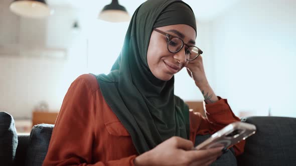 Handsome Muslim woman wearing eyeglasses texting by phone