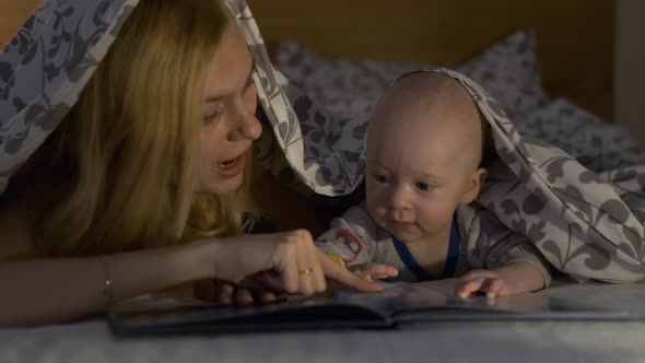 mom and son read a fairy tale hiding under a blanket in the light of a lantern