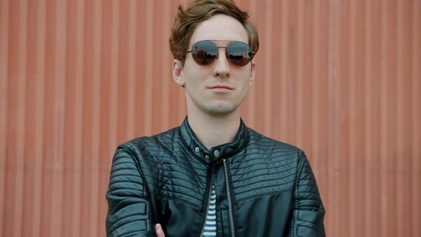 Portrait of Cool Guy Wearing Sunglasses and Leather Jacket Standing Outdoors with Arms Crossed