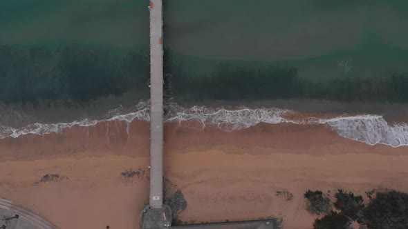 Beautiful aerial top-down static shot of empty pier from beach to sea. God's eye view