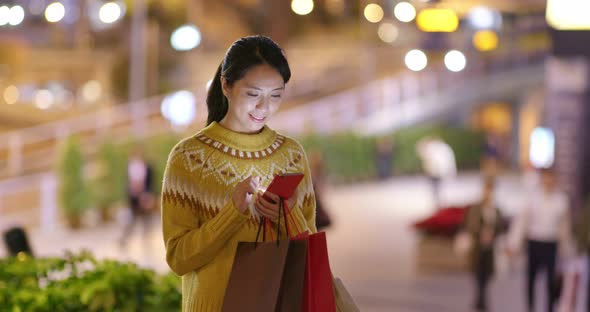 Woman use of smart phone and holding with shopping bag at night