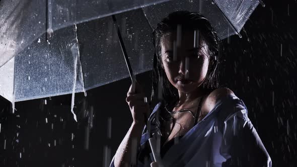 Beautiful girl in a black swimsuit and shirt. Stands in the rain, holds a transparent umbrella in hi