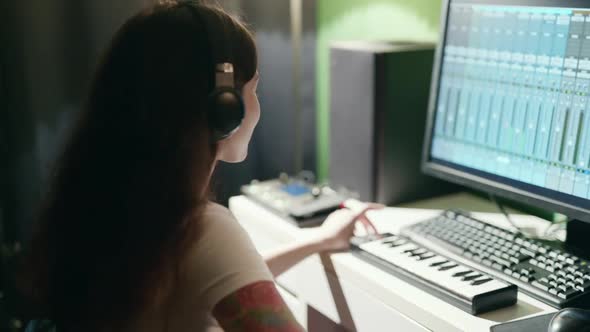 Young Woman Playing Guitar and Synthesizer Creating Music Using Equalizer Program. Female Musician