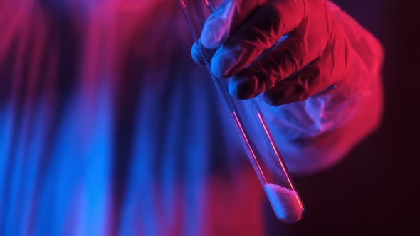 scientist in neon blue light holds test tube and pours white crystalline powder