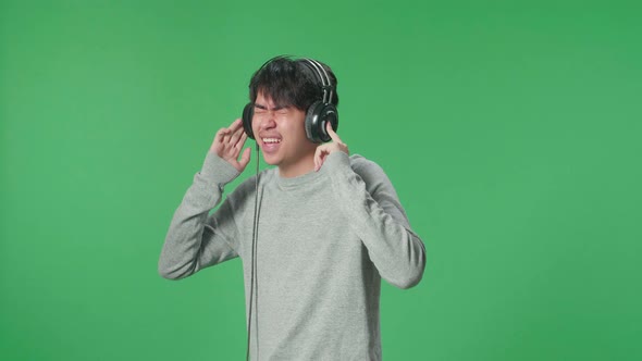 Side View Asian Man Listening To Music With Headphones And Dancing In The Green Screen Studio