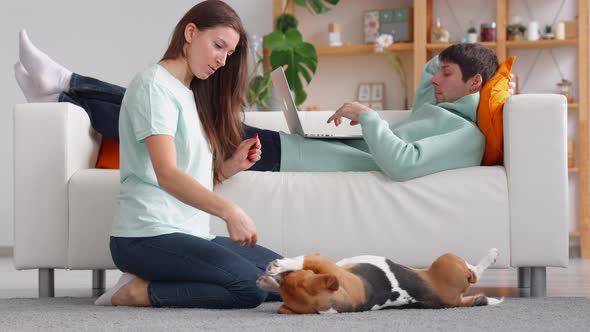 Woman Playing with Dog Man Using Laptop and Lying on Couch at Home Room Spbi