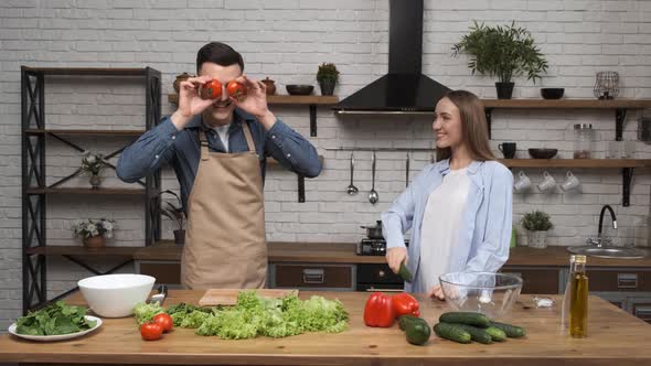 Cooking Salad at Home Young Woman and Man Laughing and Fooling Around with Vegetables in Modern