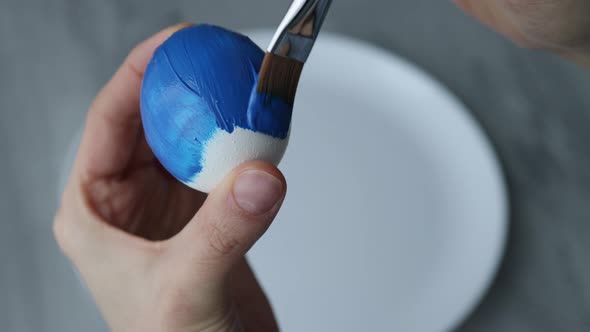 Close-up. Female hands paint Easter egg in a modern minimalist style with colorful paint.