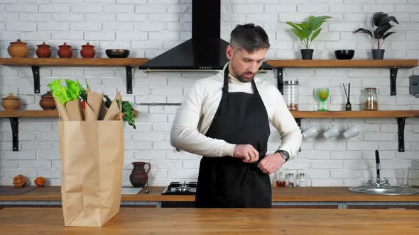 Man in sweater comes to home kitchen puts on apron preparing cook healthy food