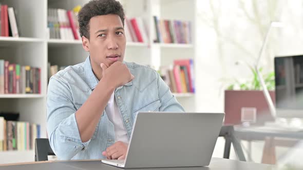 Young African American Man Thinking and Working on Laptop Brainstorming