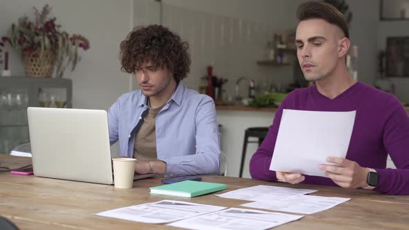 Young Gay Couple Managing Finances Reviewing Their Bank Accounts Using Laptop Computer at Home