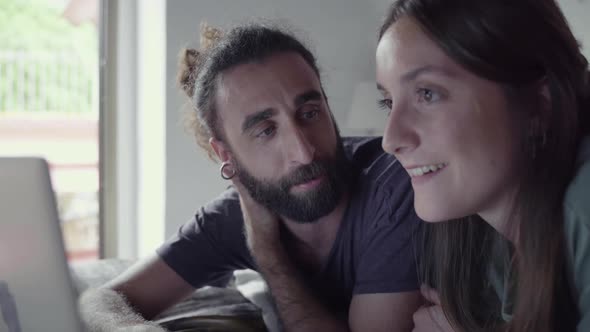 Couple lying on bed and using laptop