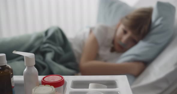 Sick Preteen Boy with Nasal Tube Lying in Hospital Bed Looking at Tray with Medication