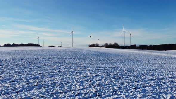 Flying above a snowy field towards a windfarm in Germany. Aerial view of a wind farm.