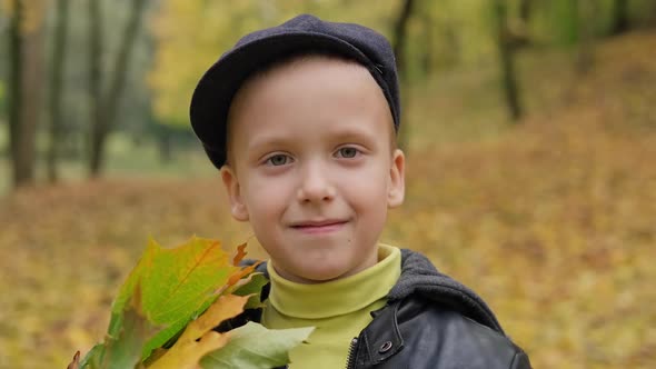 Little Boy in Cap Smiling and Looking at Camera in Autumn Park