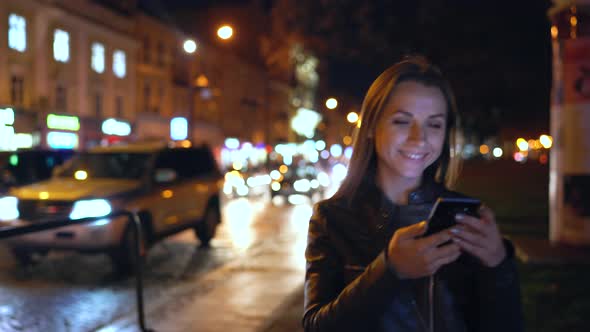 Attractive Woman Using a Smartphone While Walking Through the Streets of the Evening City