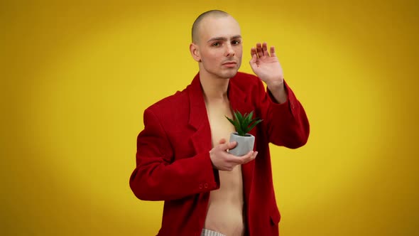 Medium Shot of Young Male Queer Holding Potted Green Plant Posing at Yellow Background in Red Jacket